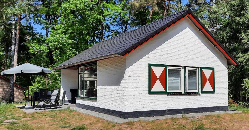 una pequeña casa blanca con cruces rojas en las ventanas en Bungalow, vrijstaand, het Vosseven nr 38 en Stramproy