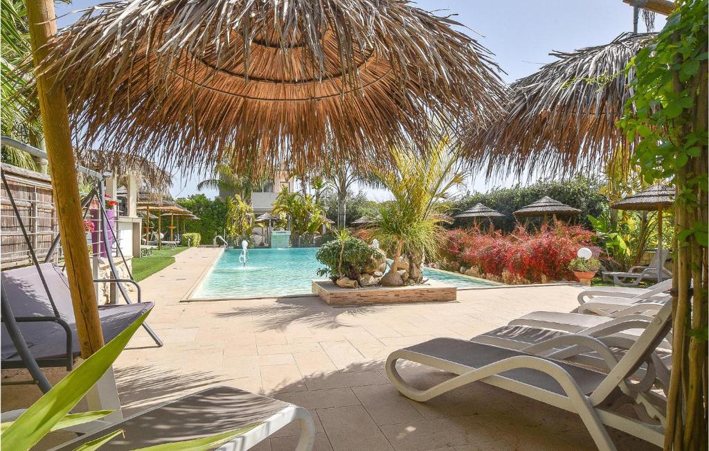 una piscina con sillas y una sombrilla de paja en Stunning Home In Pozzallo With Sauna, en Pozzallo