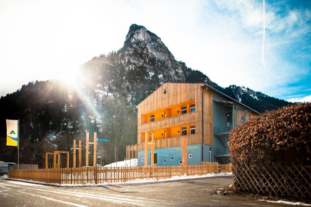 a building in front of a mountain with the sun at Jugendherberge Oberammergau in Oberammergau