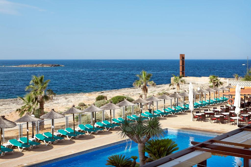 una piscina con sillas y sombrillas junto al océano en Universal Hotel Romantica en Colonia de Sant Jordi