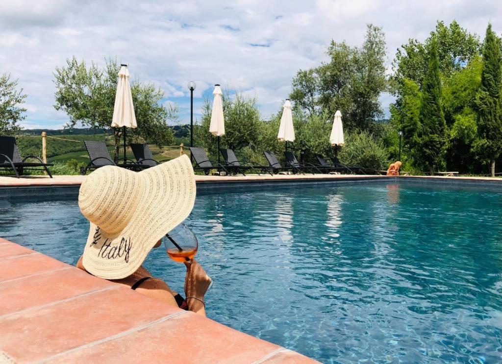 a person wearing a straw hat sitting next to a swimming pool at Agriturismo Borgo Il Bonagino in Radda in Chianti