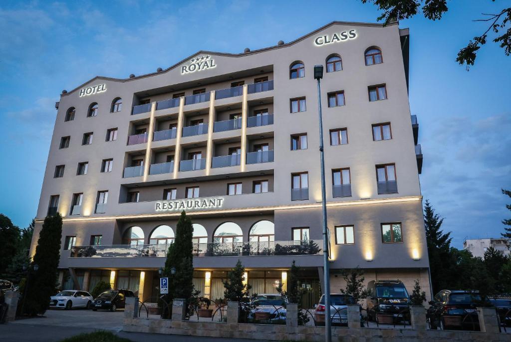 un gran edificio blanco con coches aparcados en un aparcamiento en Royal Class Hotel en Cluj-Napoca
