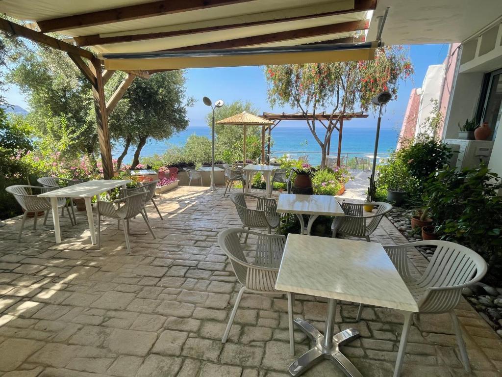 a patio with tables and chairs and the ocean in the background at Horizon Beach Hotel in Plakias