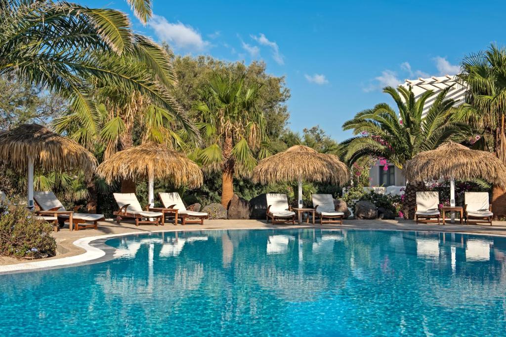 una piscina con sillas, sombrillas y palmeras en Atlantis Beach Villa, en Perivolos