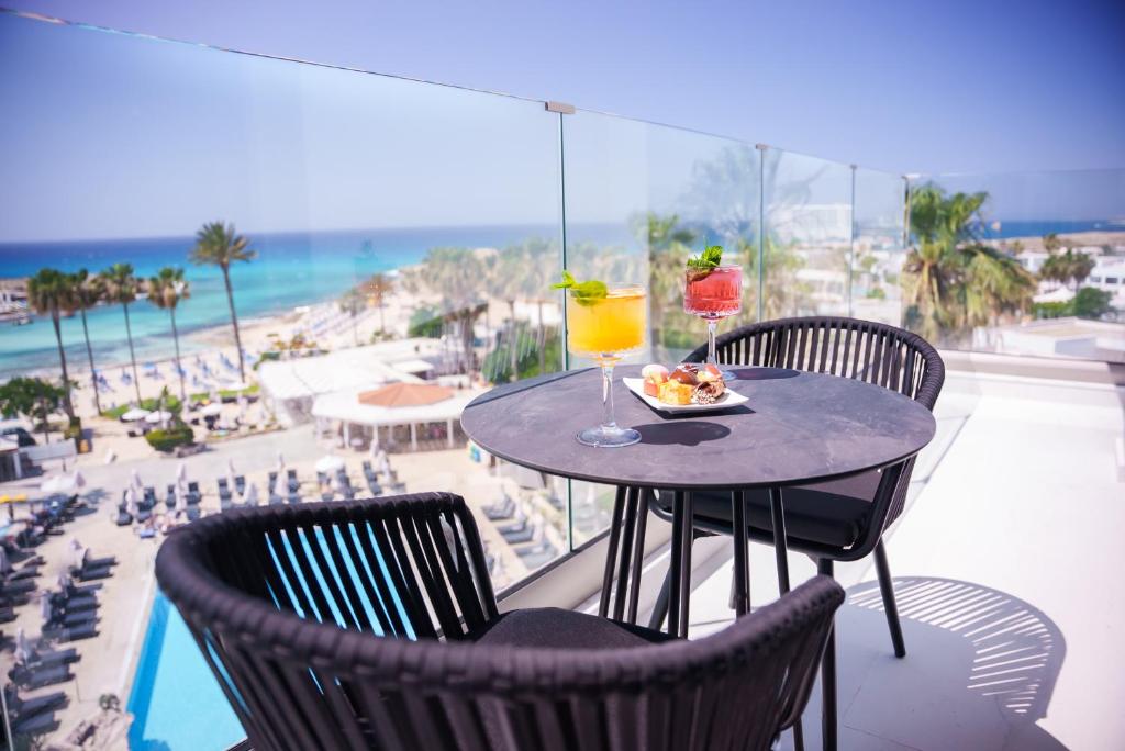 a table with a plate of food and a drink on a balcony at Pavlo Napa Beach Hotel in Ayia Napa