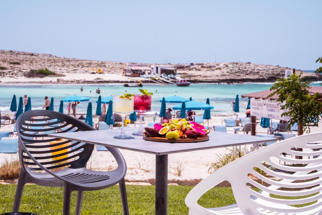 a table with a bowl of fruit and chairs on the beach at Pavlo Napa Beach Hotel in Ayia Napa