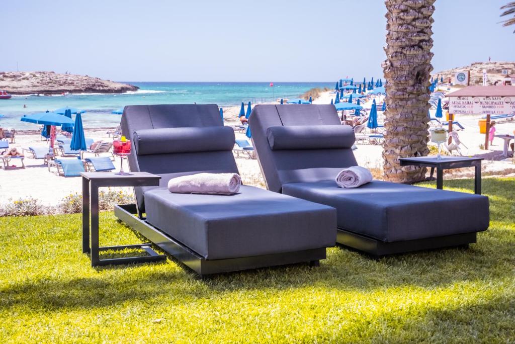 two lounge chairs sitting on the grass near the beach at Pavlo Napa Beach Hotel in Ayia Napa