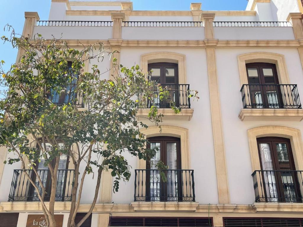 un edificio blanco con balcones y un árbol en BOUTIQUE APARTMENTS- LA GLORIA 1908, en Almería