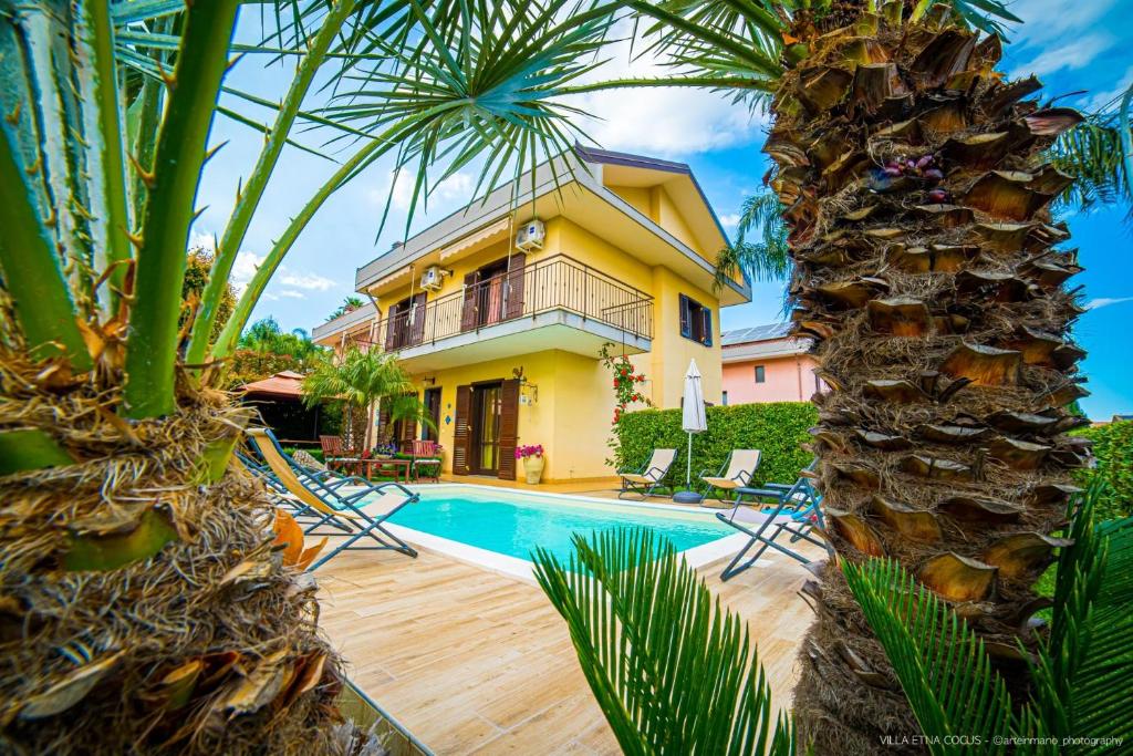 a villa with a swimming pool and palm trees at Casa vacanze ETNA COCUS in Santa Venerina