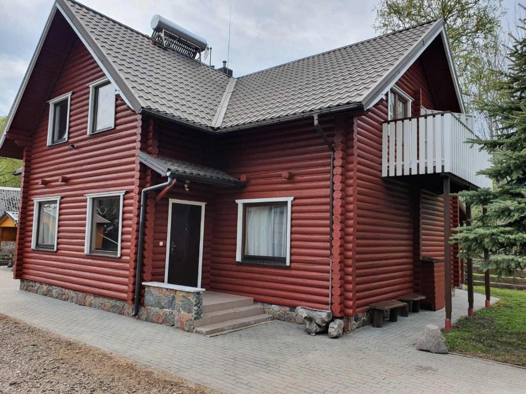 a red wooden house with a porch and a balcony at Vila Aura in Šventoji