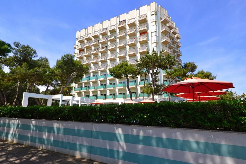 un gran edificio con una sombrilla roja delante de él en International Seaview Apartments en Lignano Sabbiadoro