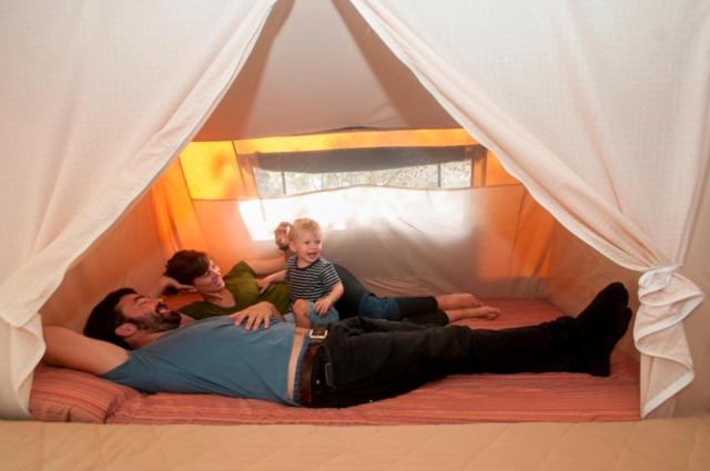 a man laying on a bed with two children in a tent at camping yaso-guara in Yaso