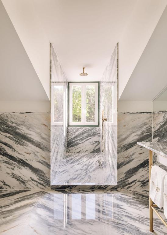 A marble-lined walk-in shower sits beneath a bright window.