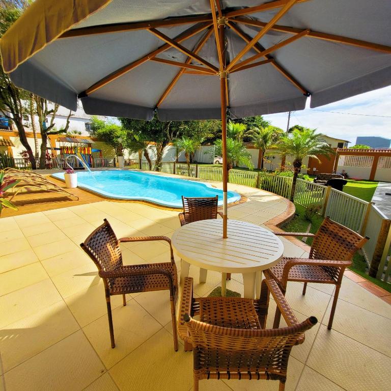 a table and chairs with an umbrella in front of a pool at Casa de praia com piscina e playground in Vila Velha