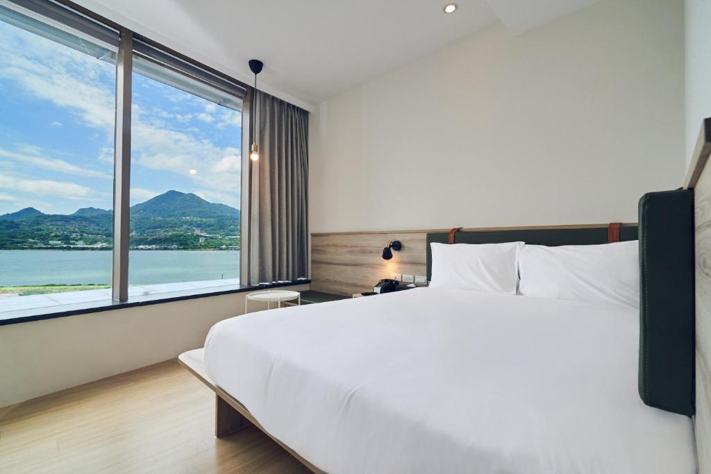 a bedroom with a large white bed and a large window at CHECK Inn Express New Taipei Tamsui in Tamsui
