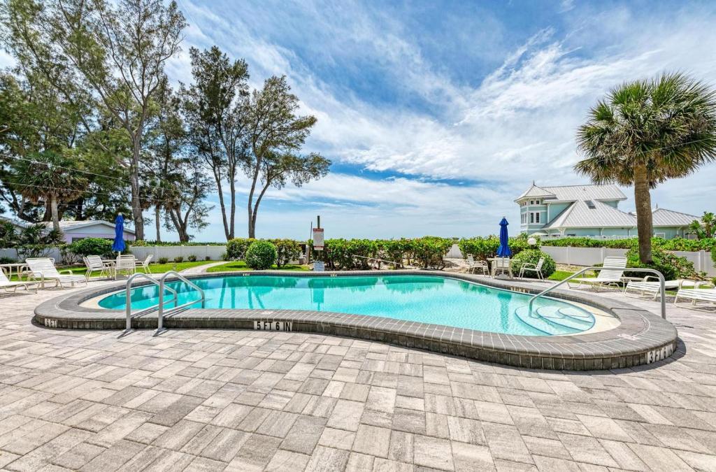 a swimming pool with chairs and trees and a house at Sunset Beach 102: Gulf Front, Stunning Views, On the Beach, Pool by Anna Maria Life Vacation Rentals in Holmes Beach