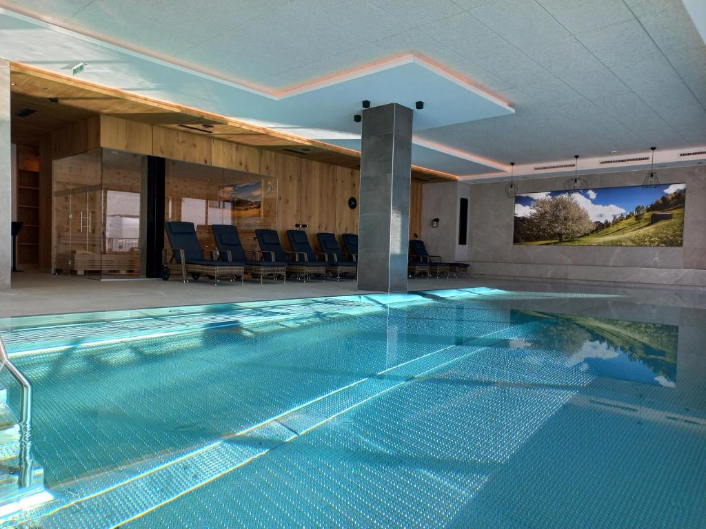 a large swimming pool in a house with chairs at Hotel Alpenroyal in Fiss