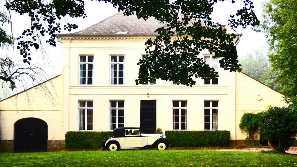 une vieille voiture garée devant une maison blanche dans l'établissement Maison De Plumes, à Heuchin