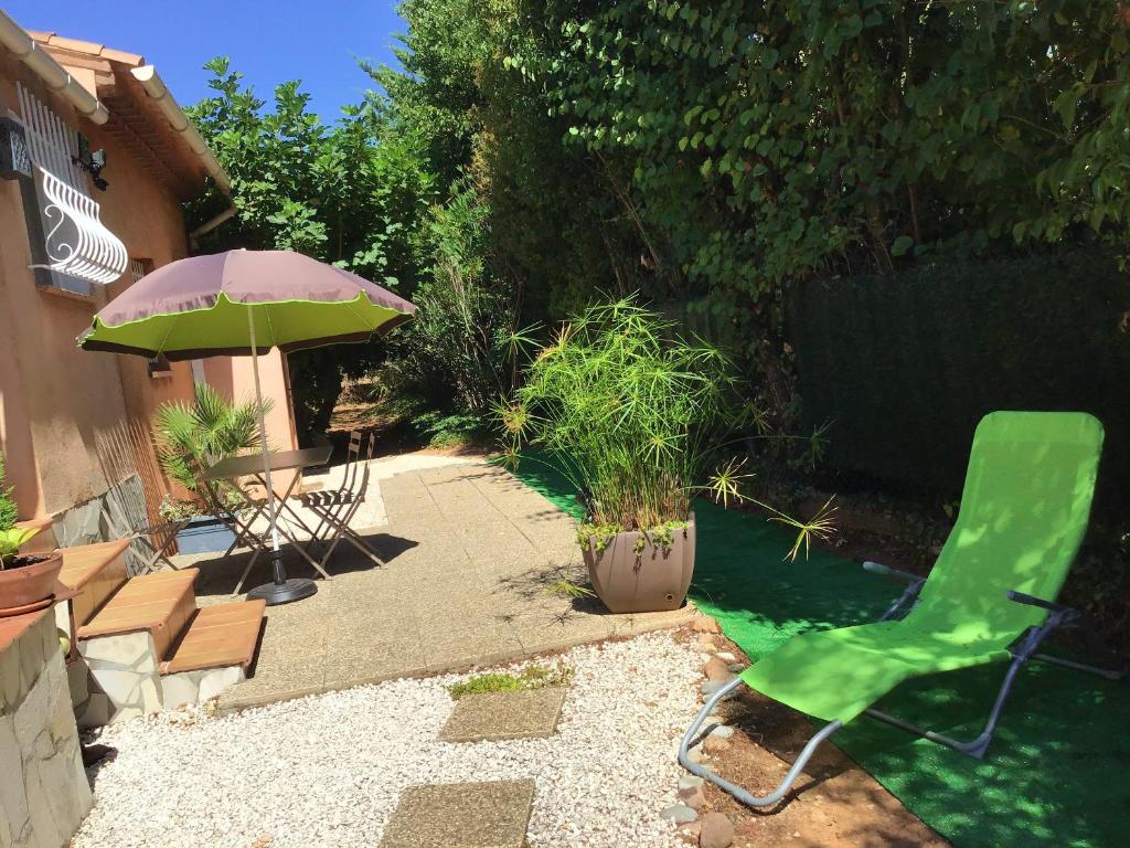 une terrasse avec une chaise verte et un parasol dans l'établissement Charmant appartement à Le Muy avec terrasse et jardin, au Muy