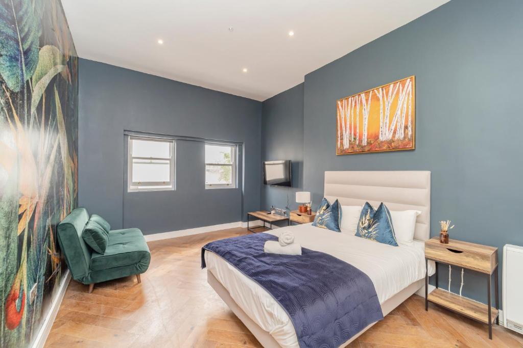 1 dormitorio con paredes azules, 1 cama y 1 silla verde en NEW *SPACIOUS STUDIO *HIGH CEILING * MINS AWAY FROM BRIGHTON BEACH, en Brighton & Hove
