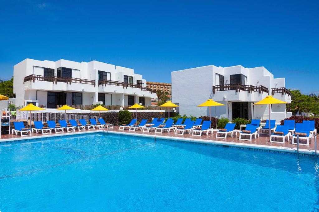 a swimming pool with chairs and umbrellas in front of a hotel at Paraiso del Sol y Paradero in Playa de las Americas