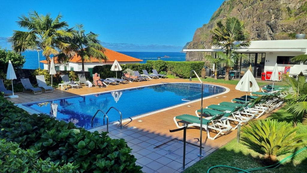 uma piscina num resort com cadeiras e o oceano em Casa da Capelinha em Ponta Delgada