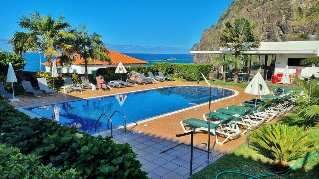 a pool at a resort with chairs and the ocean at Casa da Capelinha in Ponta Delgada