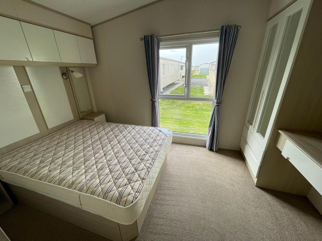 a small bedroom with a bed and a window at PG177 Golden Palm Resort 8 Berth Caravan With Decking in Chapel Saint Leonards