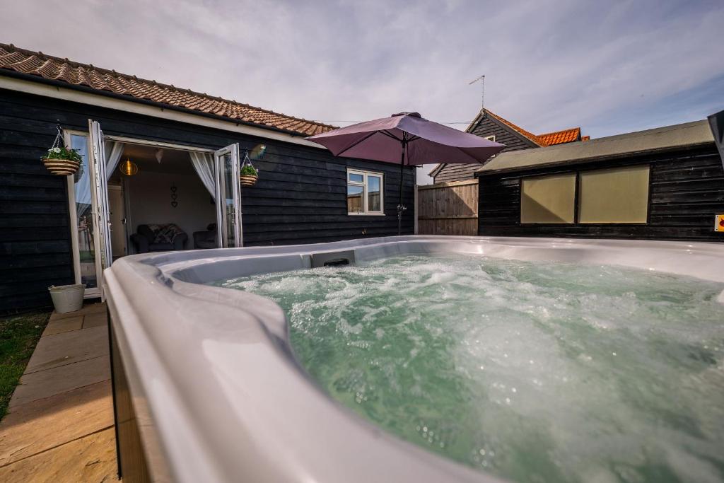 a hot tub in front of a house with an umbrella at The Stables in Halesworth