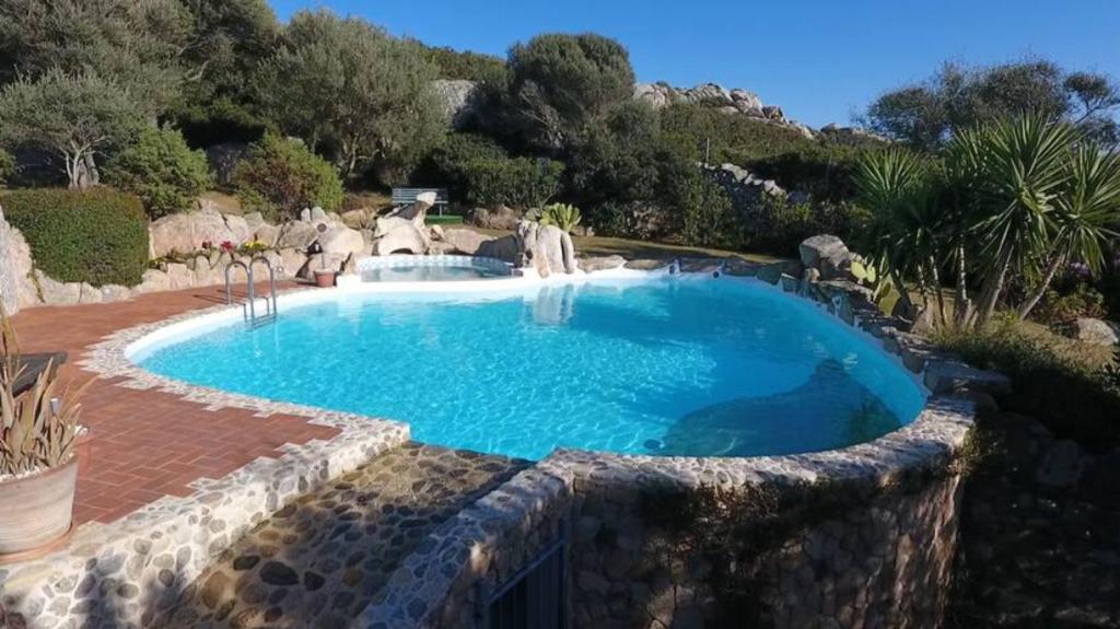 a swimming pool in a yard with a stone wall at Sardinia Family Villas - Villa Elena with salt water private pool in Arzachena