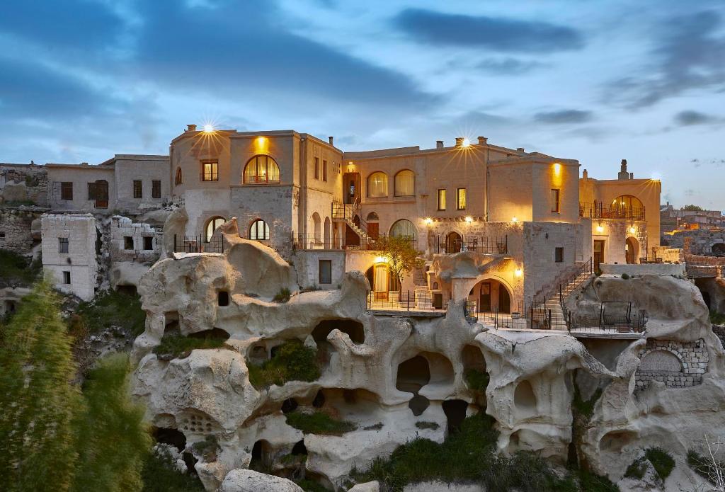a large building on a cliff with a mountain at Charm Of Cappadocia Cave Suites in Nevşehir