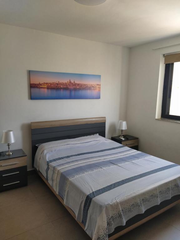 ein Schlafzimmer mit einem Bett, zwei Tischen und einem Gemälde an der Wand in der Unterkunft Perfect value apartment in St Paul's Bay