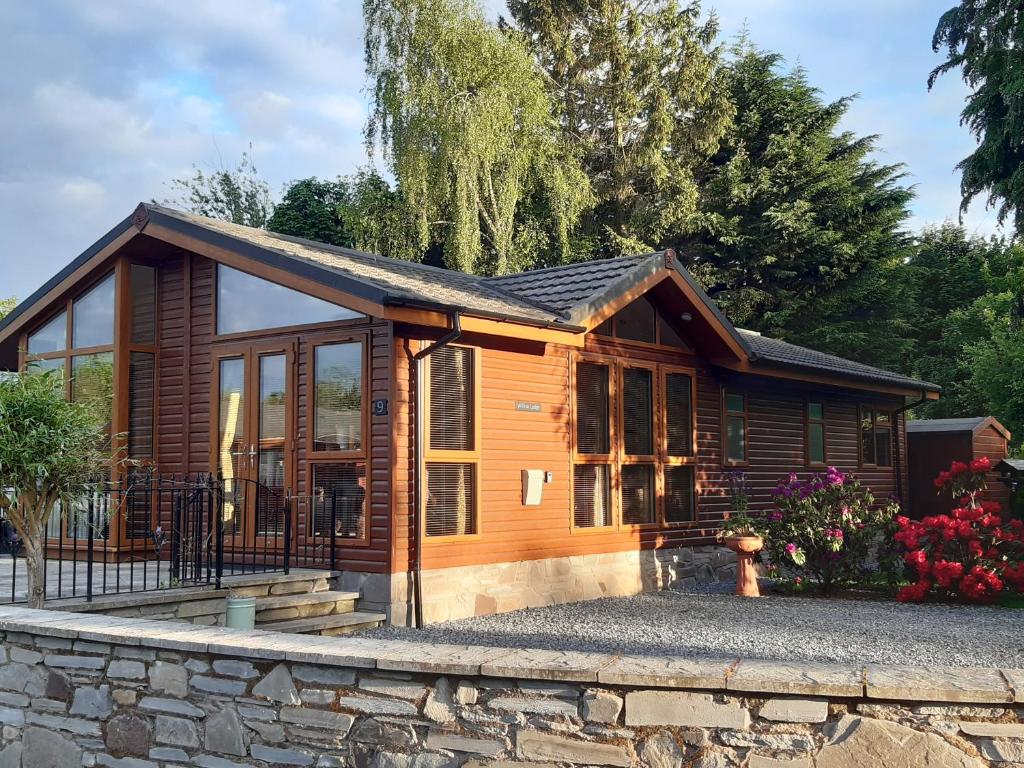 a wooden cabin with a stone wall at Willow Lodge Auchterarder in Auchterarder