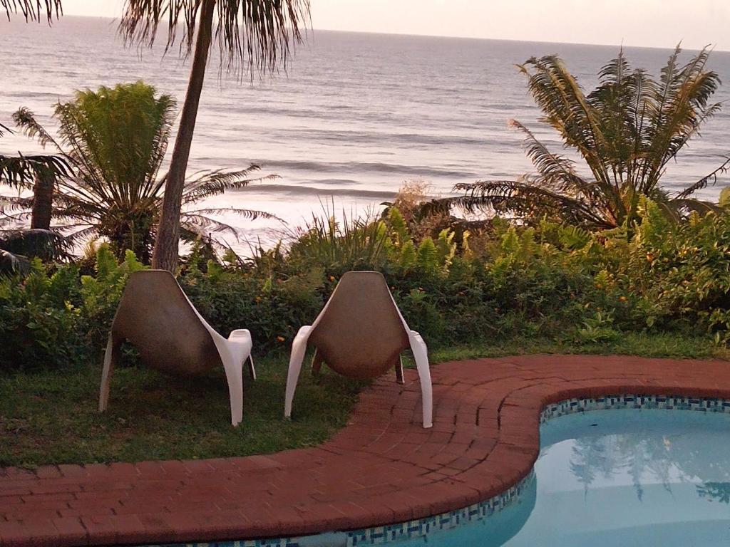 dwa krzesła siedzące przy basenie w pobliżu oceanu w obiekcie Whispering Waves w mieście Bazley Beach
