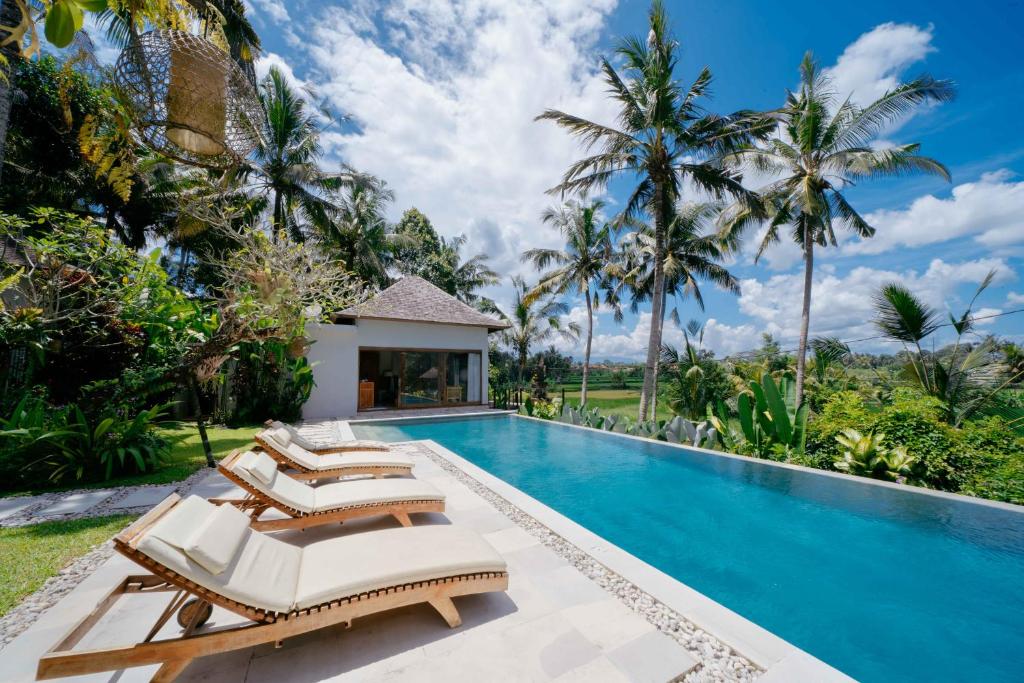 a swimming pool with two beds and palm trees at Santun Luxury Private Villas-CHSE CERTIFIED in Ubud