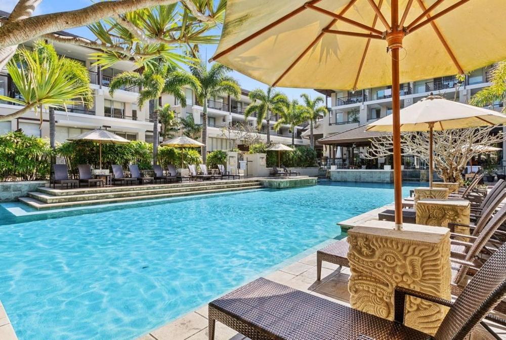 a swimming pool with chairs and umbrellas next to a building at Santai Resort - Holiday Management in Kingscliff
