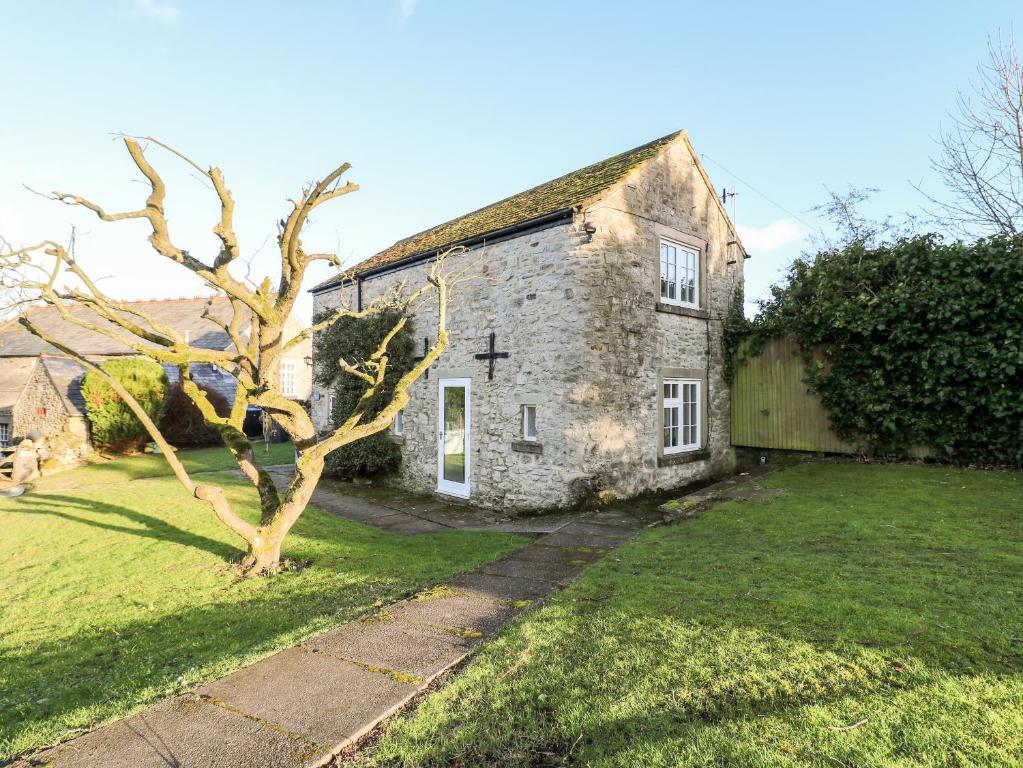 eine alte Steinkirche mit einem Baum im Hof in der Unterkunft Manor Barn Cottage in Bakewell