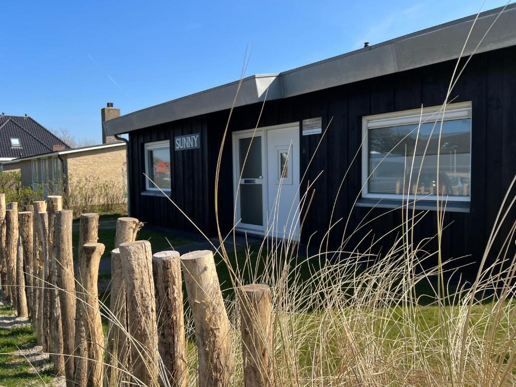 a black tiny house sitting next to a fence at Bungalow Sunny, lekker uitwaaien op het strand! in Callantsoog