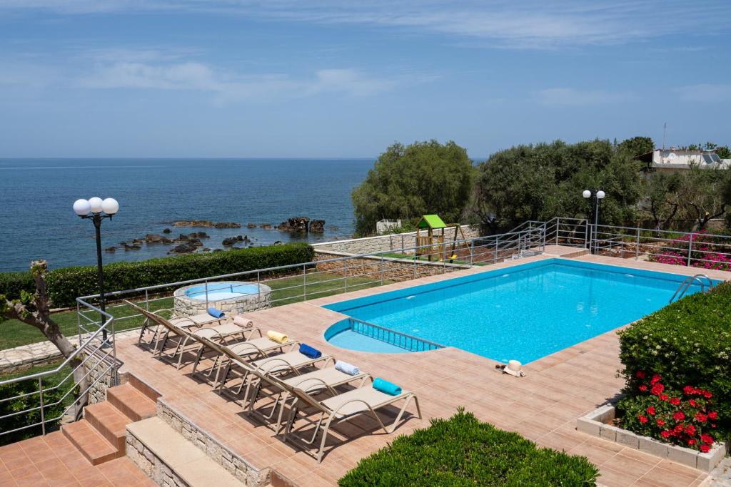 a swimming pool with chairs and the ocean in the background at Beachfront Family Villa Katerina with Private pool, Playground, BBQ & Amazing Sea Views! in Petres