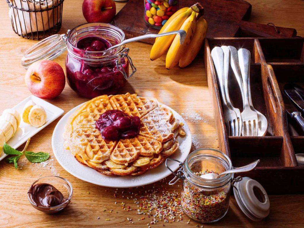 a table topped with a plate of waffles and fruit at ibis München Parkstadt Schwabing in Munich