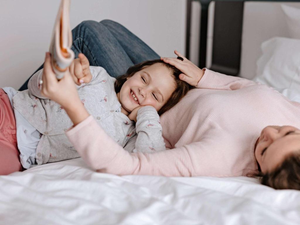 a woman laying in bed with a little girl reading a book at ibis München Parkstadt Schwabing in Munich