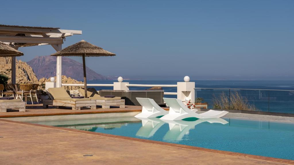 a pool with white chairs and a view of the ocean at Arkasa Palace in Arkasa