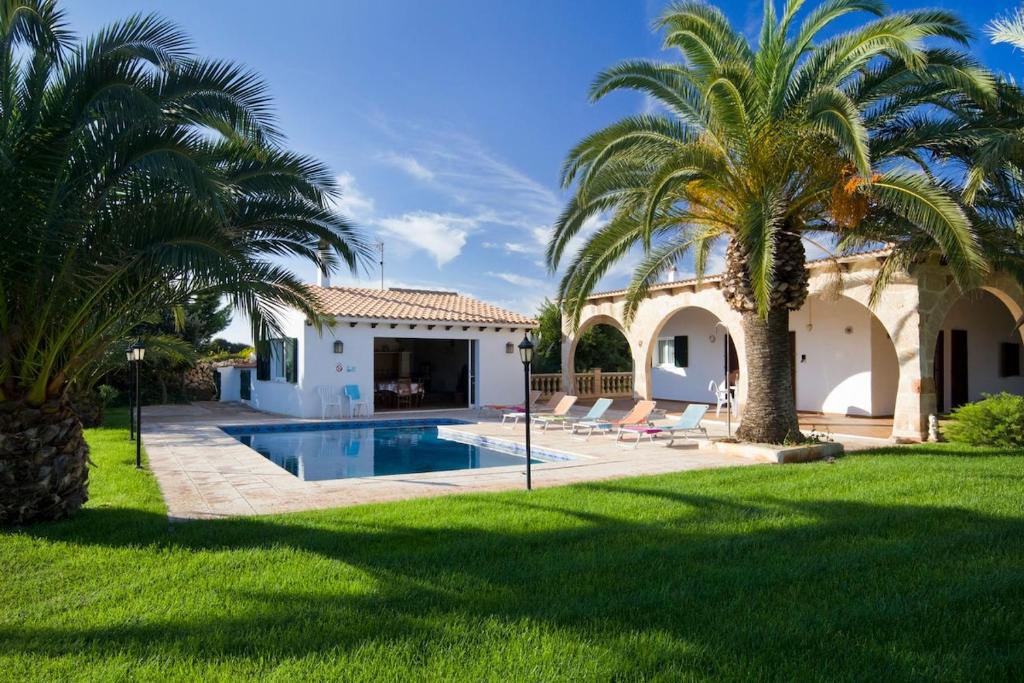 a villa with a swimming pool and palm trees at Villa S'Hortal in Ciutadella