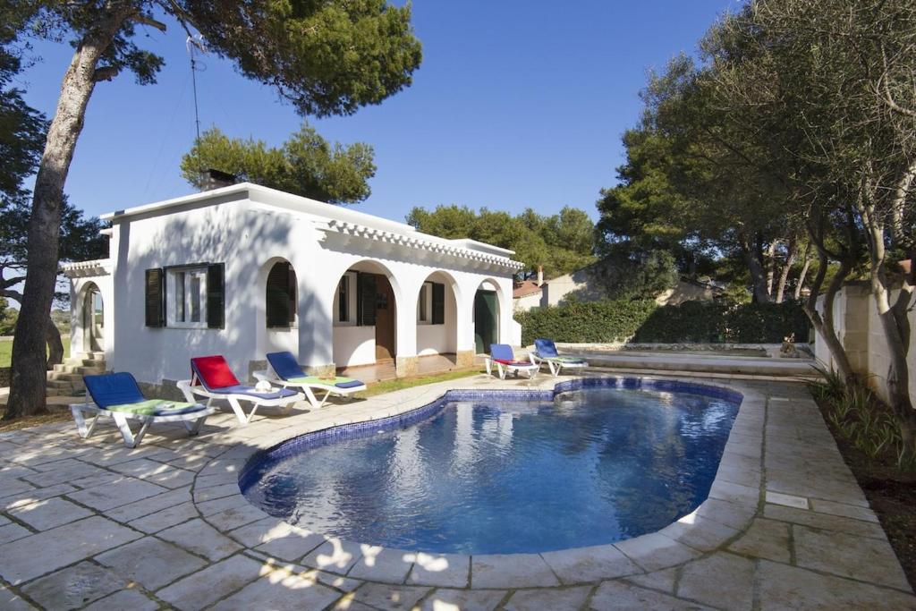 a swimming pool with chairs and a house at Villa Gregal in Cala Blanca