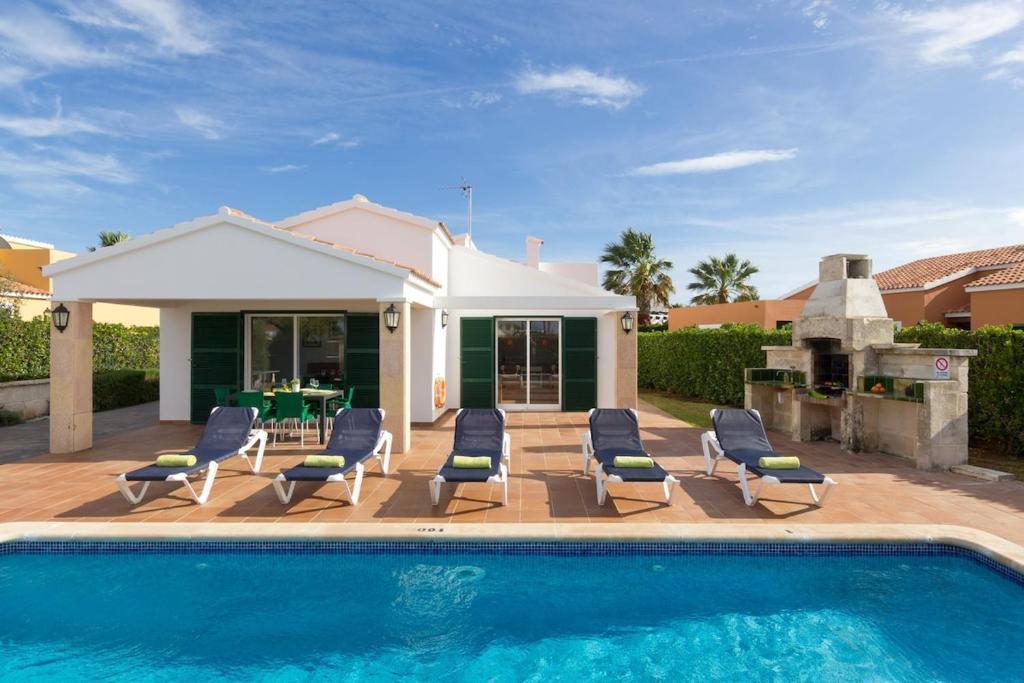 a swimming pool with chairs and a house at Villa S'Aladern in Cala'n Bosch