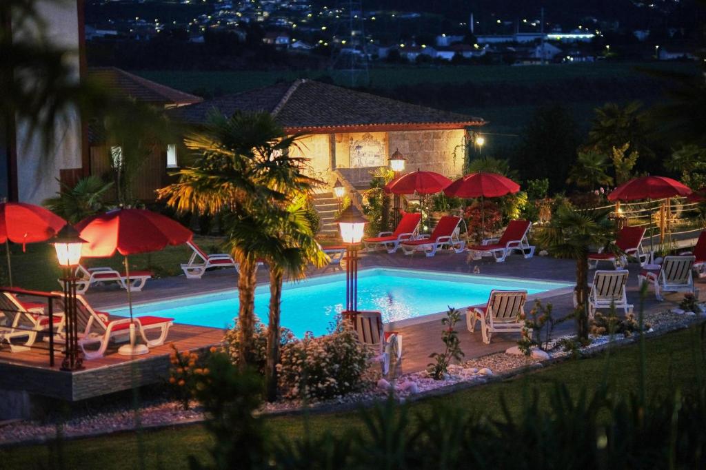 a swimming pool with chairs and umbrellas at night at Aldeia da Quinta do Paço in Santo Tirso
