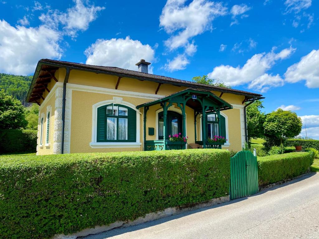 uma pequena casa amarela com uma sebe verde em Cottage am Attersee em Nussdorf am Attersee