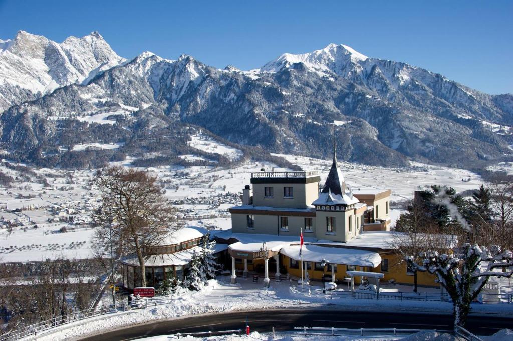 a building covered in snow with mountains in the background at Komplettes Hotel mit 10 Zimmern in Bad Ragaz