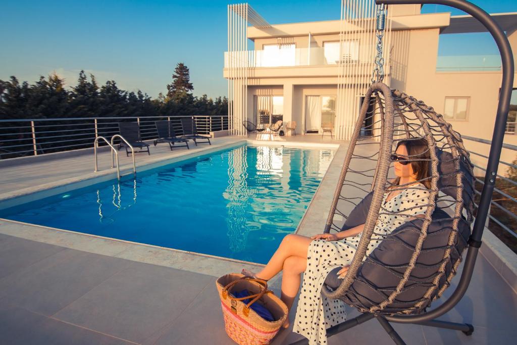 a woman sitting on a swing by a swimming pool at IO Luxury Pool & Hot Tub Suites in Preveza