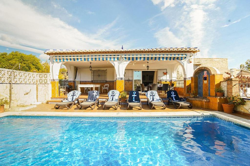 a swimming pool with chairs and a house at Villa Triana in Nerja